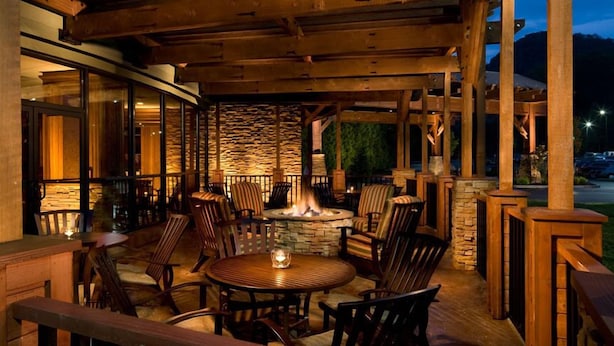 An outdoor patio with wooden beams, stone walls, and a fire pit surrounded by chairs and tables. - The Park Vista - a DoubleTree by Hilton Hotel - Gatlinburg (Gatlinburg)