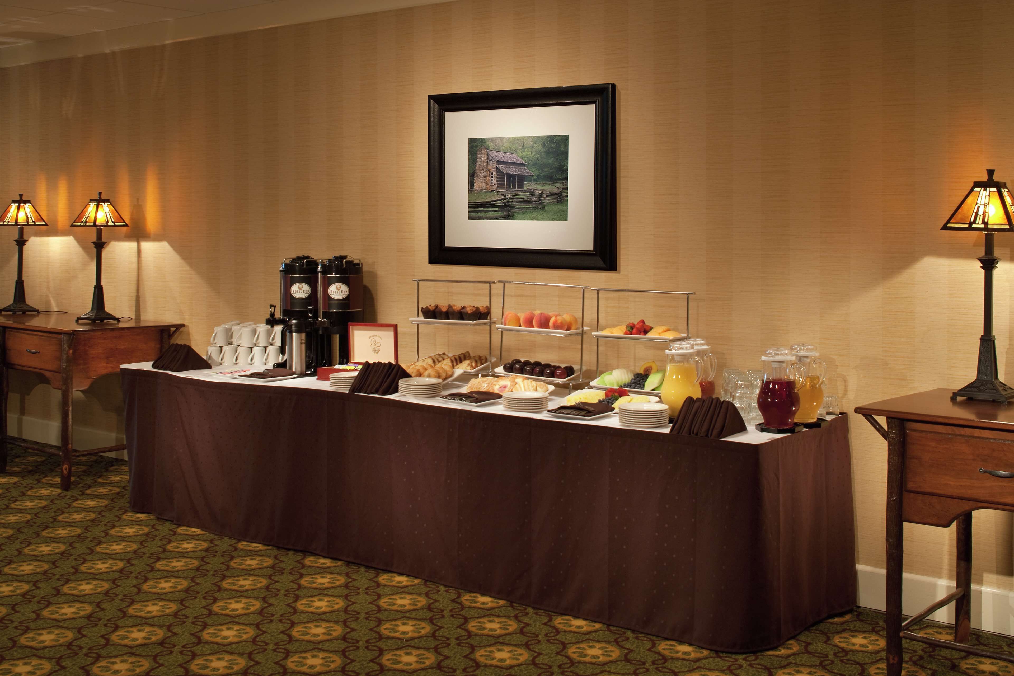 A buffet setup with various food items and beverages, a framed picture on the wall, and two lamps on either side.