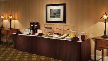 A buffet setup with various food items and beverages, a framed picture on the wall, and two lamps on either side.
