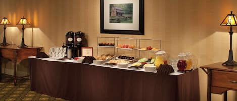 A buffet setup with various food items and beverages, a framed picture on the wall, and two lamps on either side.