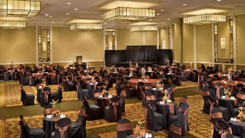 Un amplio salón de banquetes con mesas y sillas redondas, un escenario y suelo alfombrado.