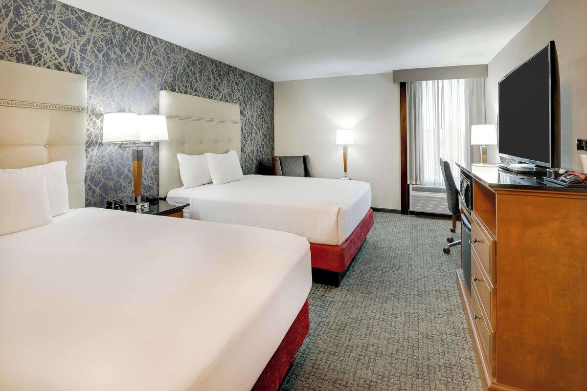 A hotel room with two beds, a TV, a desk, and a dresser.