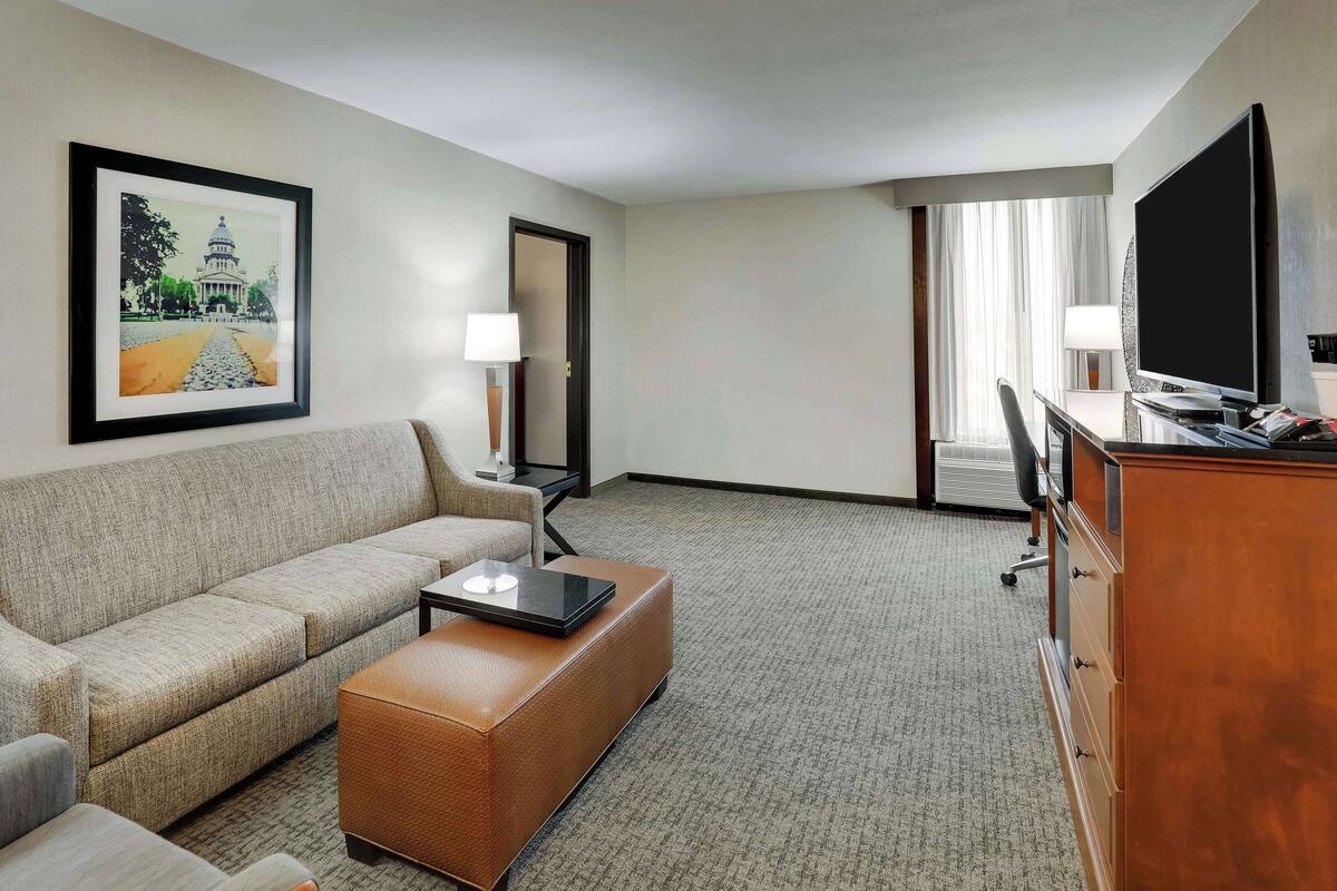 A hotel room with a sofa, a coffee table, a TV, a desk, and a lamp.