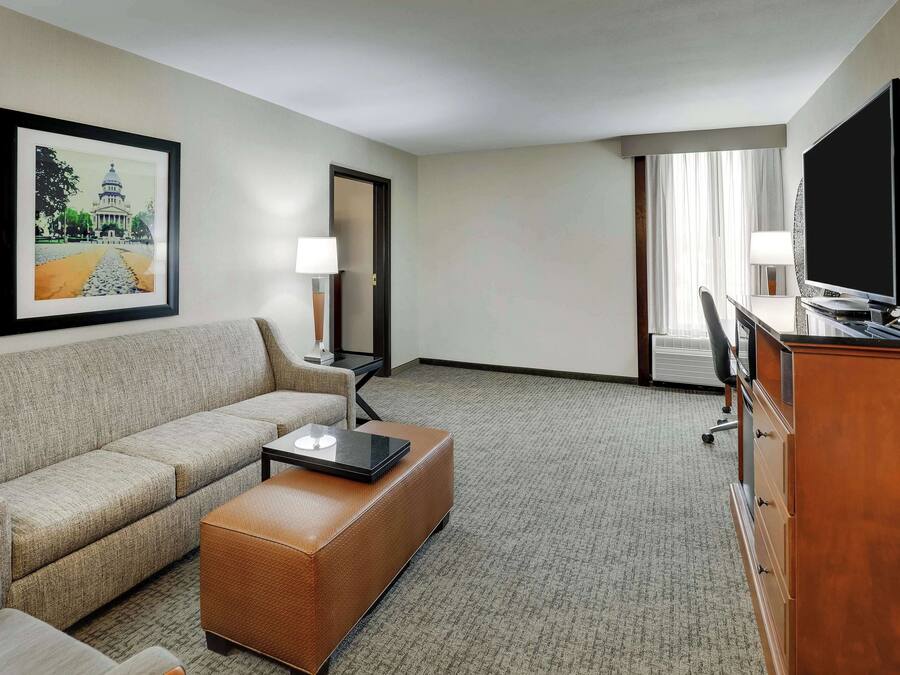A hotel room with a sofa, a coffee table, a TV, a desk, and a lamp.