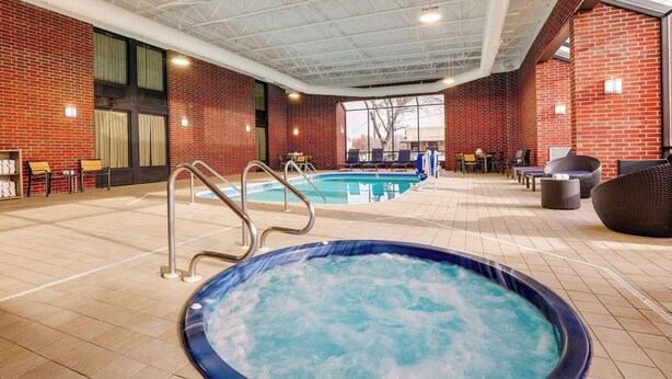 An indoor swimming pool area with a hot tub, seating, and a view of the outside. - Drury Inn & Suites Springfield IL (Springfield)