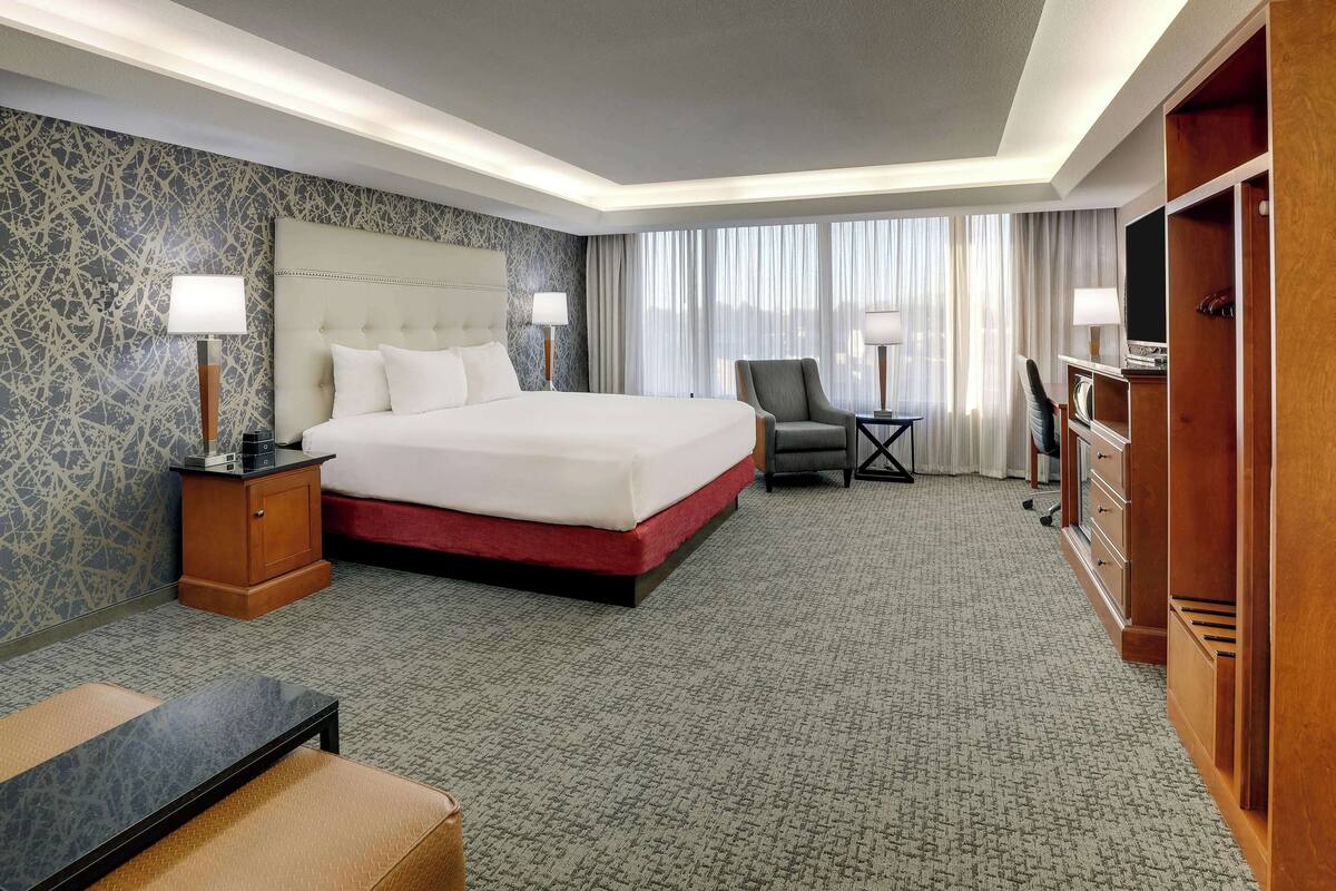 A hotel room with a large bed, a desk, a chair, and a TV.