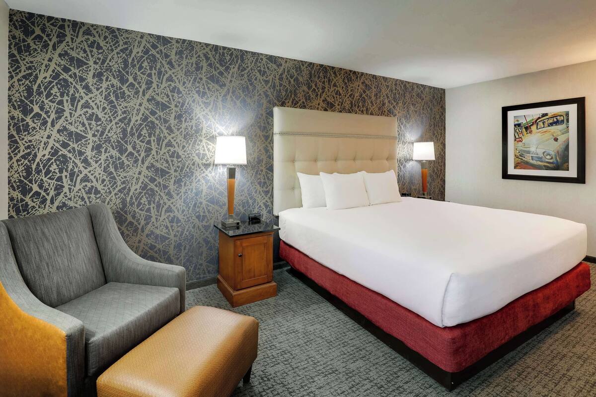 A hotel room with a large bed, a chair, a nightstand, and a lamp.