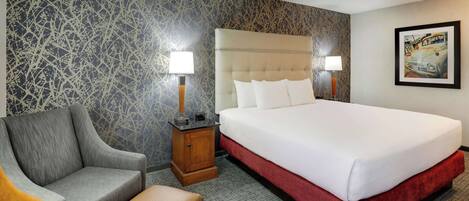 A hotel room with a large bed, a chair, a nightstand, and a lamp.