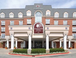 Un hotel DoubleTree Suites con fachada de ladrillo, amplias ventanas en arco y una entrada central con columnas.