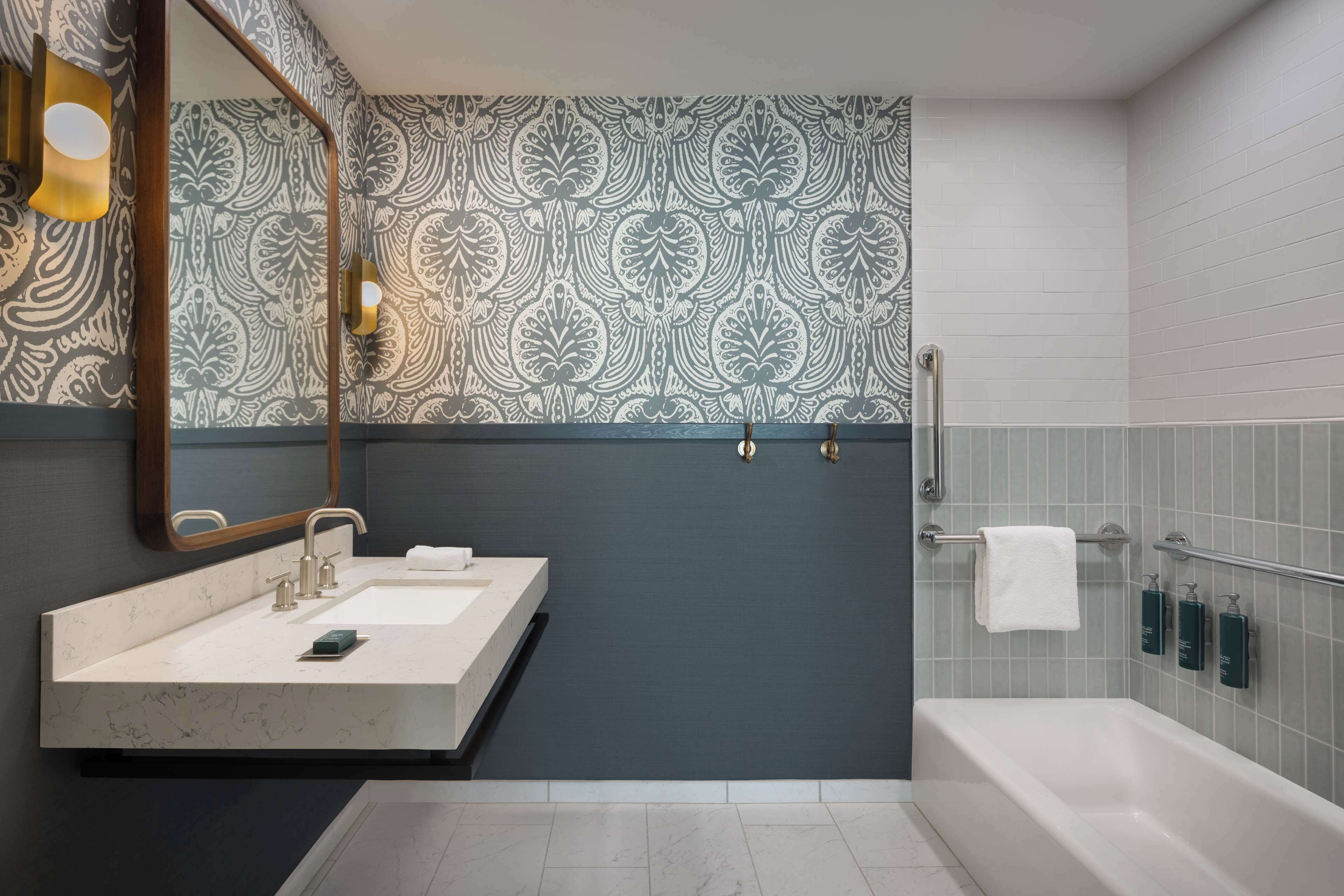 A modern bathroom with a marble sink, a large mirror, patterned wallpaper, and a bathtub.