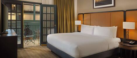 A hotel room with a large bed, two bedside lamps, a framed picture on the wall, and a view of the outdoor area through a door.
