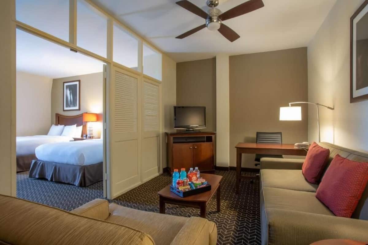 A hotel room with a bed, a desk, a television, a coffee table with snacks, and a ceiling fan.