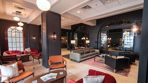 Un vestíbulo amplio con diversas opciones de asientos, incluyendo sofás, sillones y una mesa de centro. Se observan varias luminarias y un espejo grande que refleja el interior.