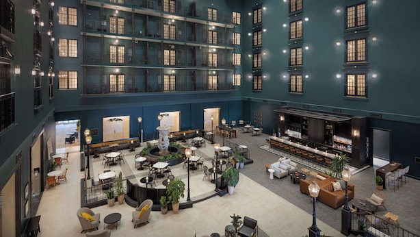 Un amplio vestíbulo de hotel con varias zonas de estar, un bar y una fuente central.