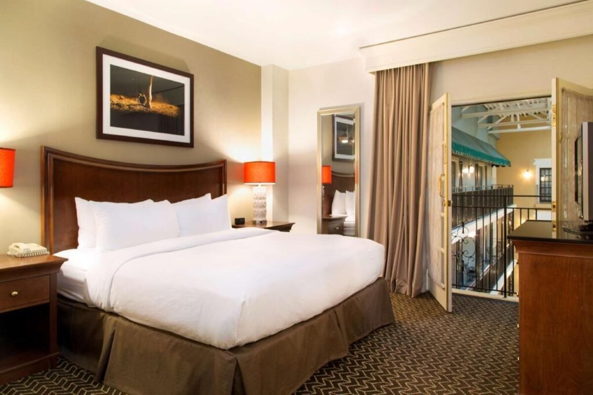 A hotel room with a large bed, bedside lamps, a telephone, a framed picture on the wall, and a view of the outside balcony.