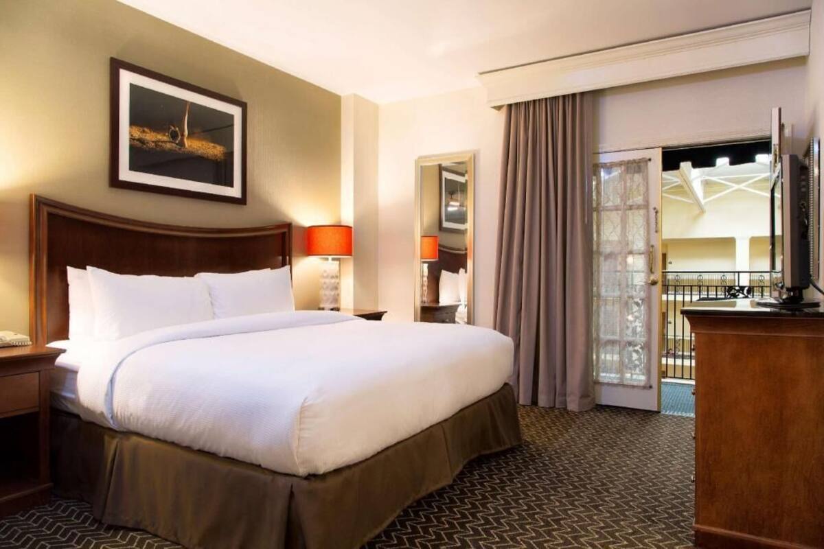 A hotel room with a large bed, a desk, a chair, a television, and a balcony with a view.