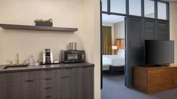A hotel room with a kitchenette, a flat-screen TV, a bed, and a view through a sliding door.