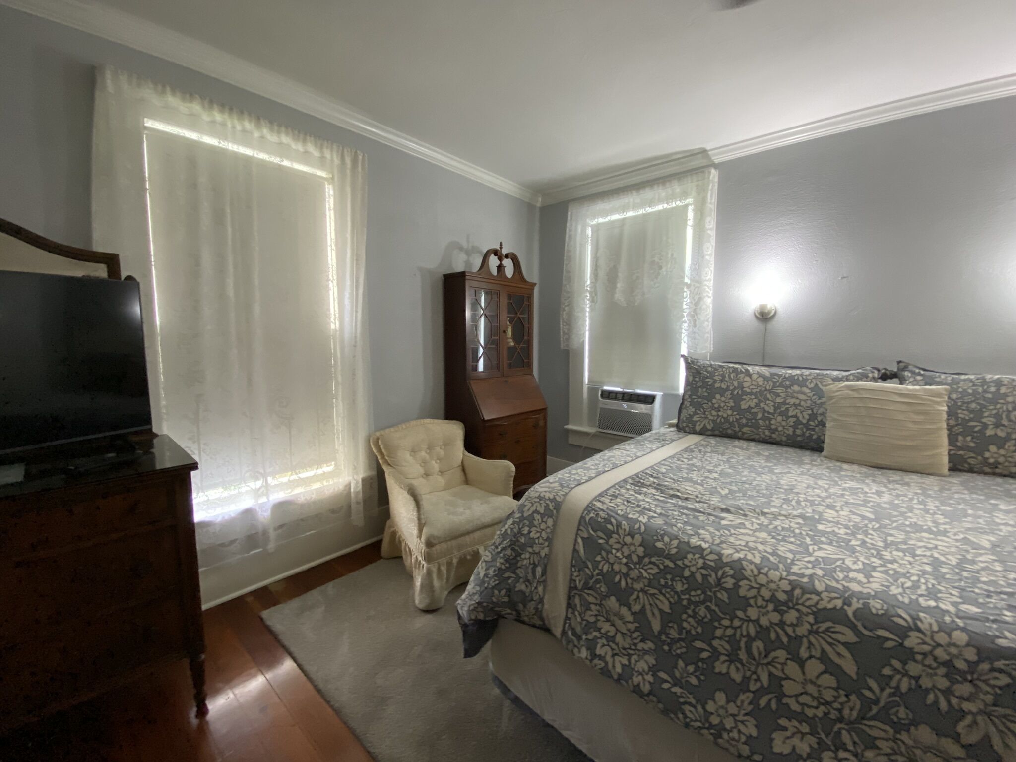 A bedroom with a bed, a chair, a dresser, a television, and a window with curtains.