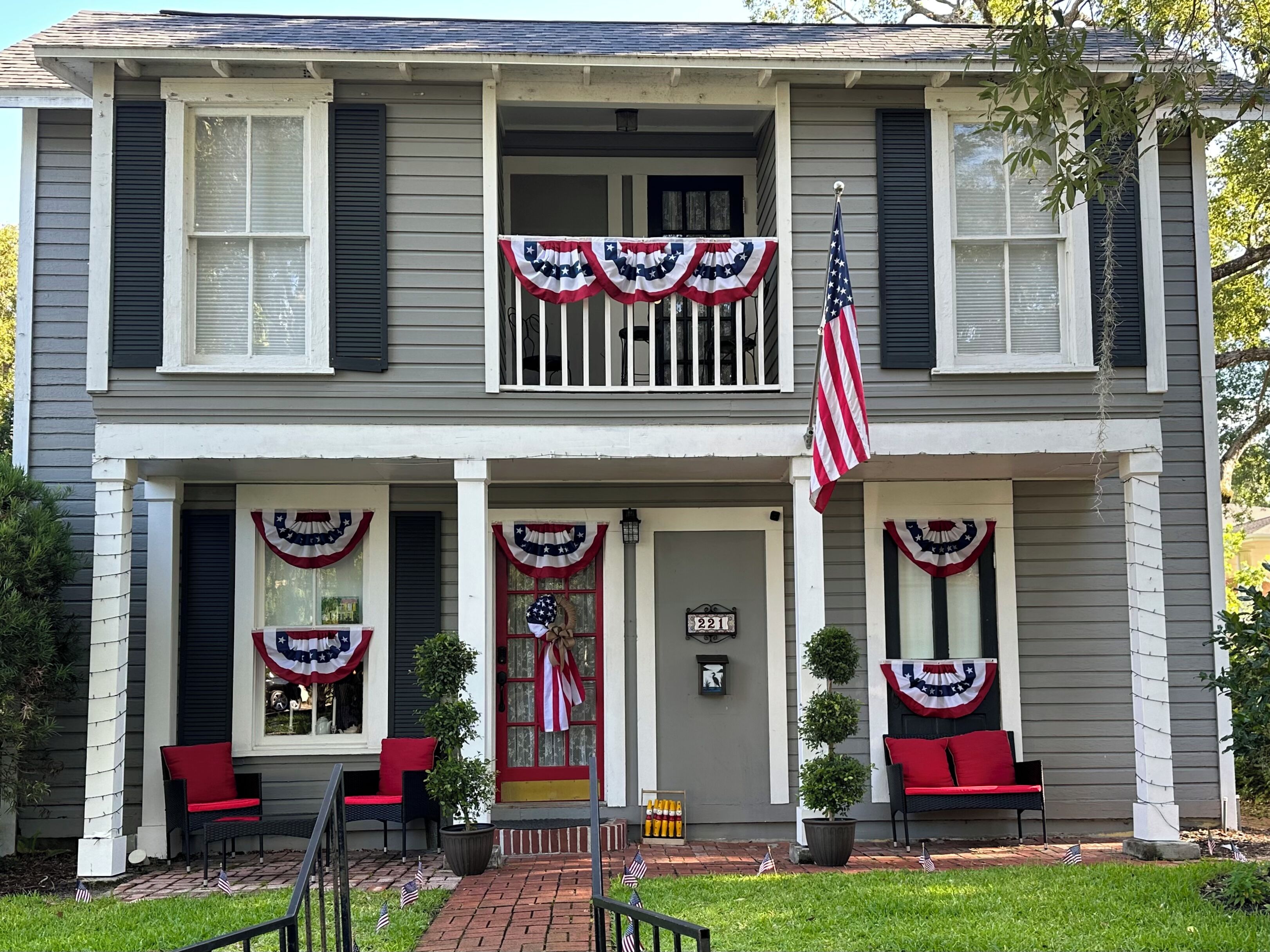A two-story house with a front porch decorated with American flags and red, white, and blue bunting.