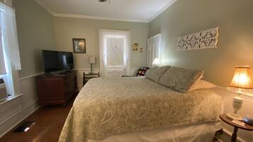 A bedroom with a bed, a television on a dresser, a ceiling fan, and a door with a window.