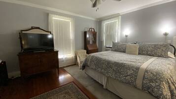Une chambre à coucher comprenant un lit, une commode, un téléviseur, un ventilateur de plafond et une fenêtre avec des rideaux.