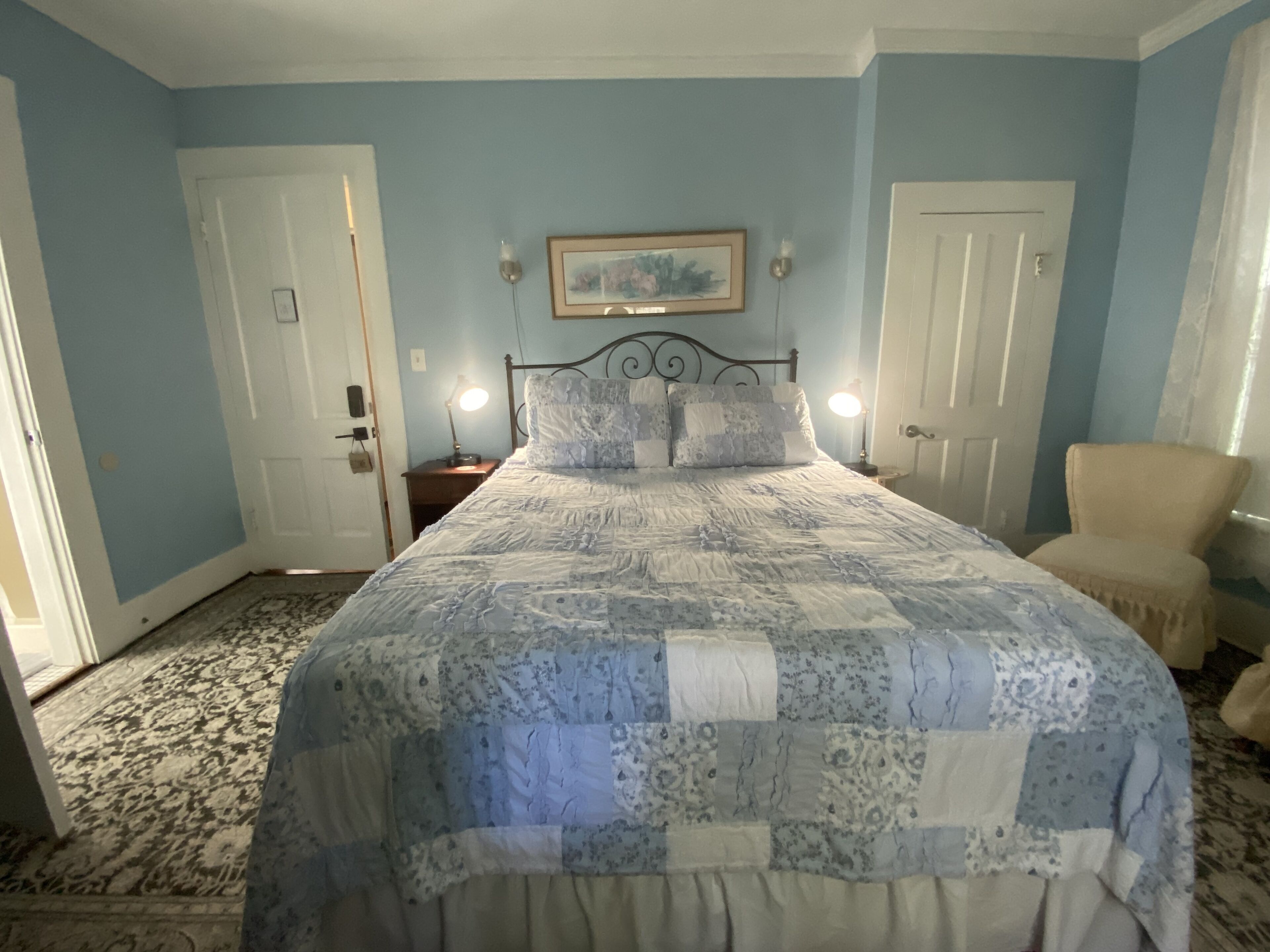 Un dormitorio con una cama, dos mesitas de noche, una silla y una puerta.