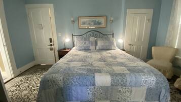 Un dormitorio con una cama, dos mesitas de noche, una silla y una puerta.
