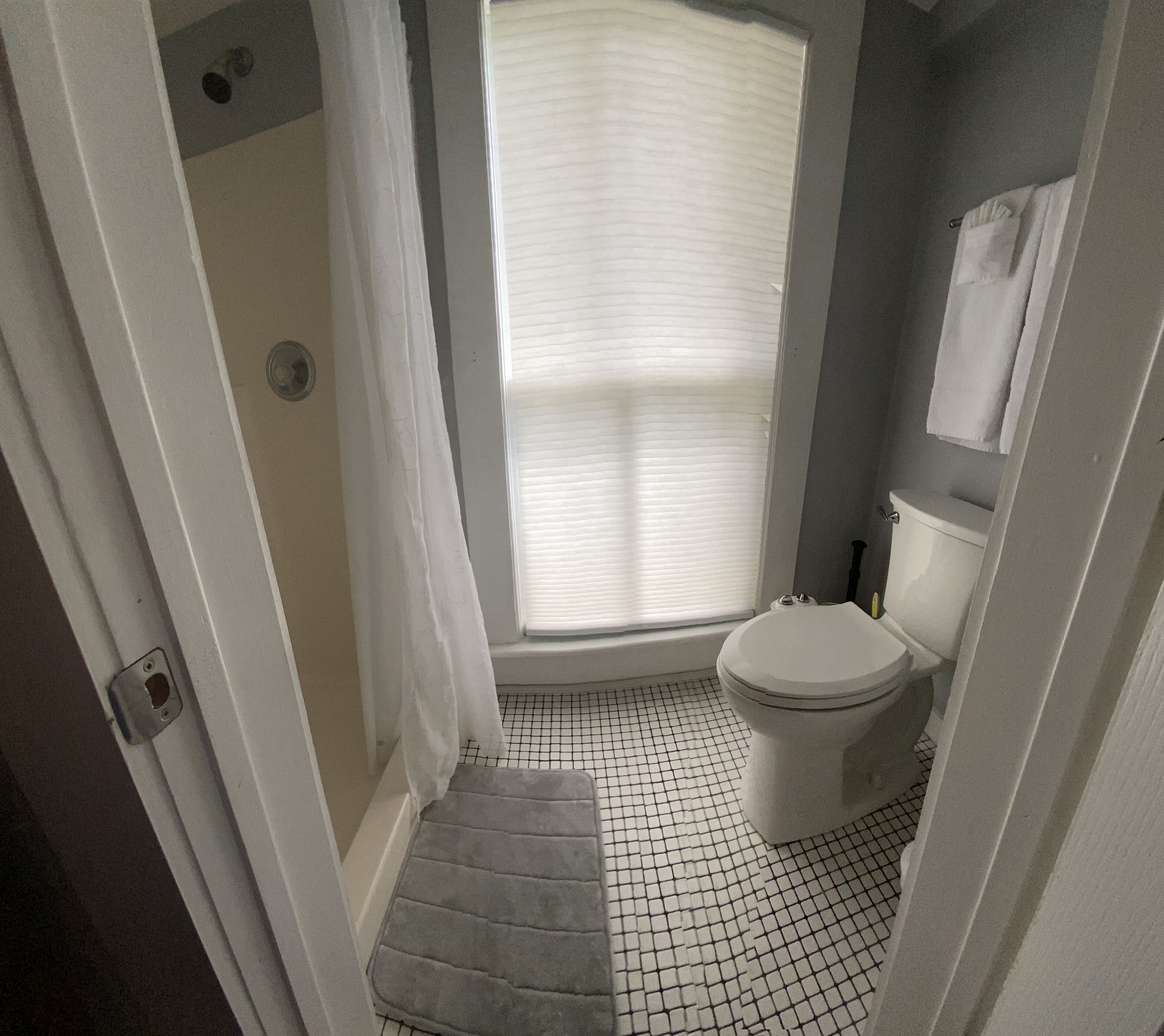 Un baño con inodoro, ducha y ventana con persianas.