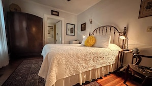 Une chambre à coucher avec un lit en bois, une literie blanche, une table de chevet avec une lampe, une chaise et un tapis à motifs.