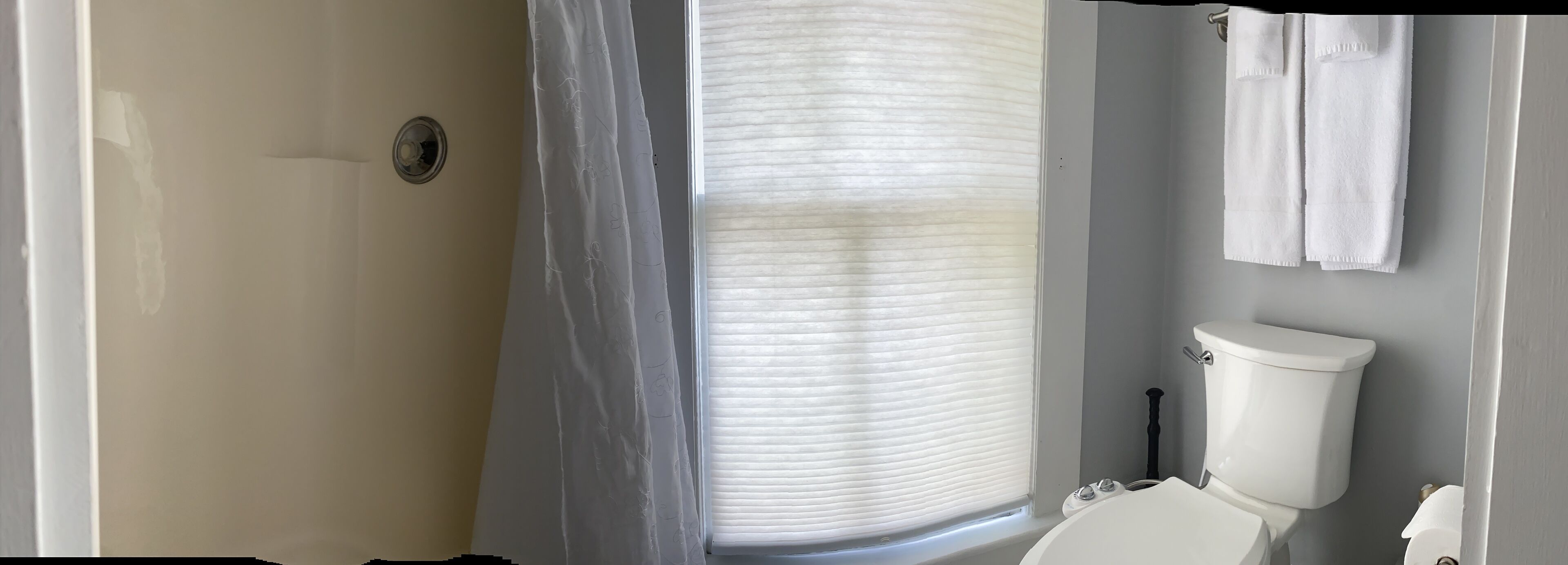 A bathroom with a shower, toilet, and window with blinds.