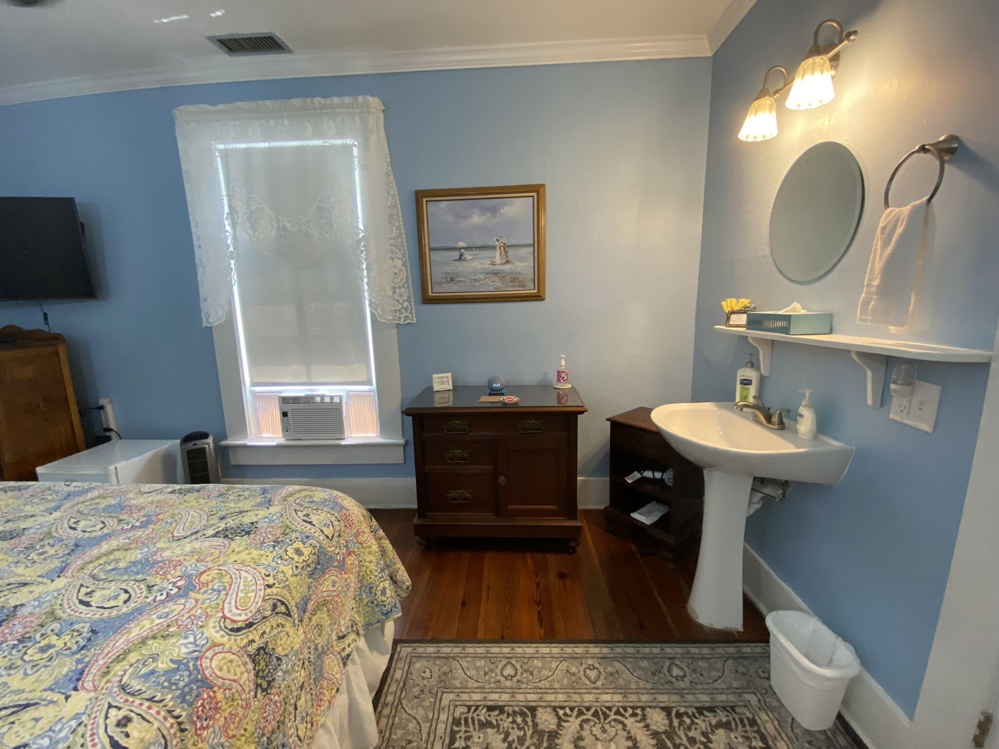 Un dormitorio con cama, cómoda, tocador y ventana con cortinas.