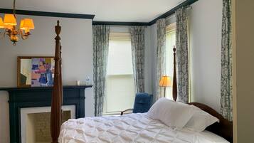 A bedroom with a four-poster bed, a fireplace, a blue chair, and a chandelier.