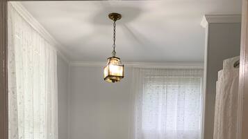 A bathroom with a toilet, a window with a curtain, and a hanging light fixture.