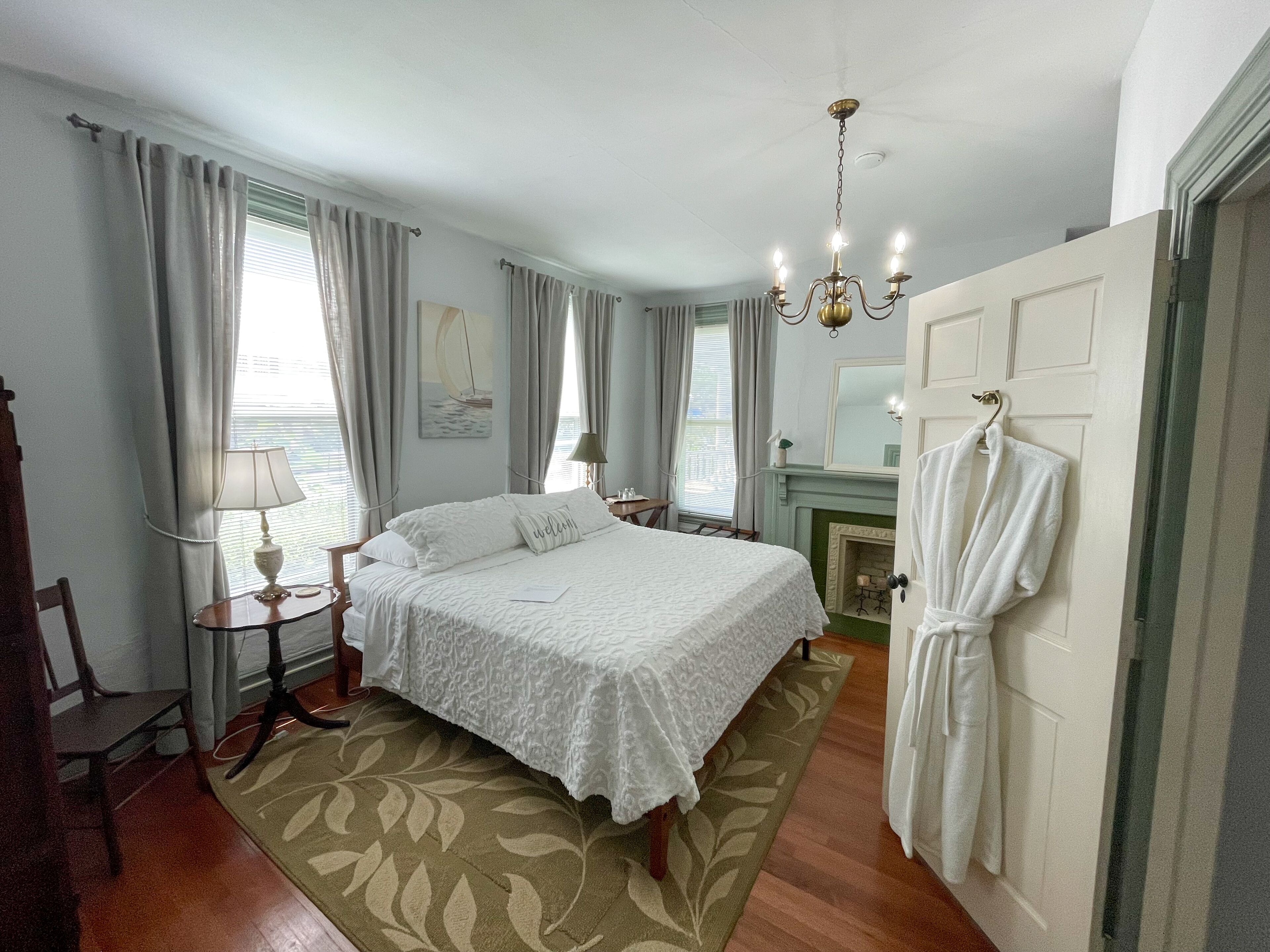 A bedroom with a bed, a bedside table, a lamp, a fireplace, a robe, and a door.