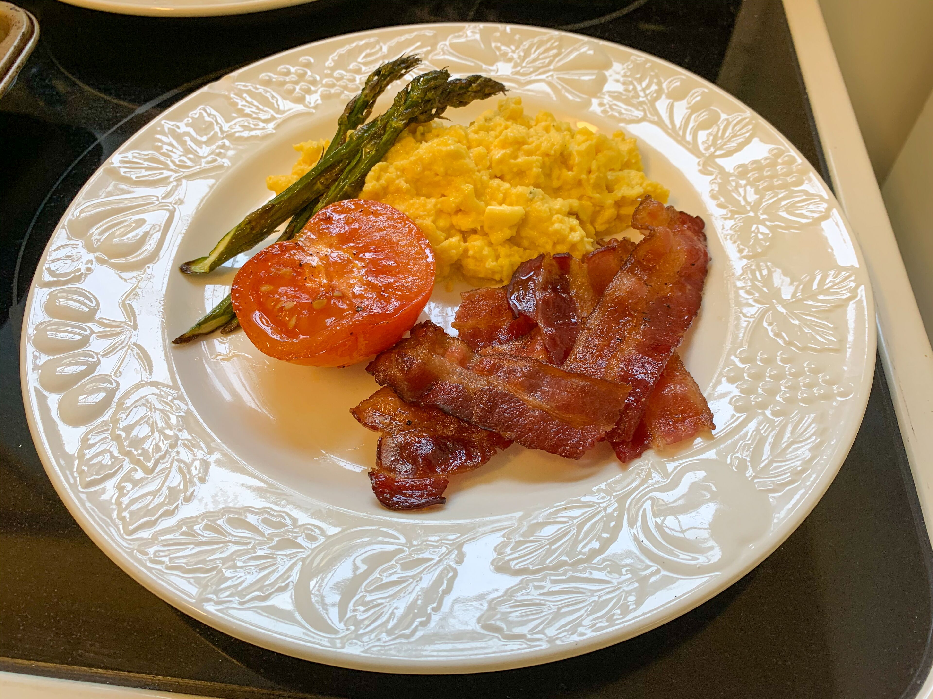Un plat amb ous barrejats, bacon, espàrrecs i una làmina de tomàquet.