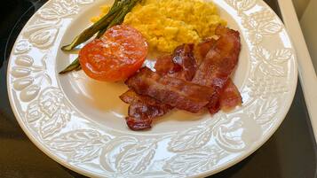 Un plato con huevos revueltos, tocino, espárragos y una rodaja de tomate.