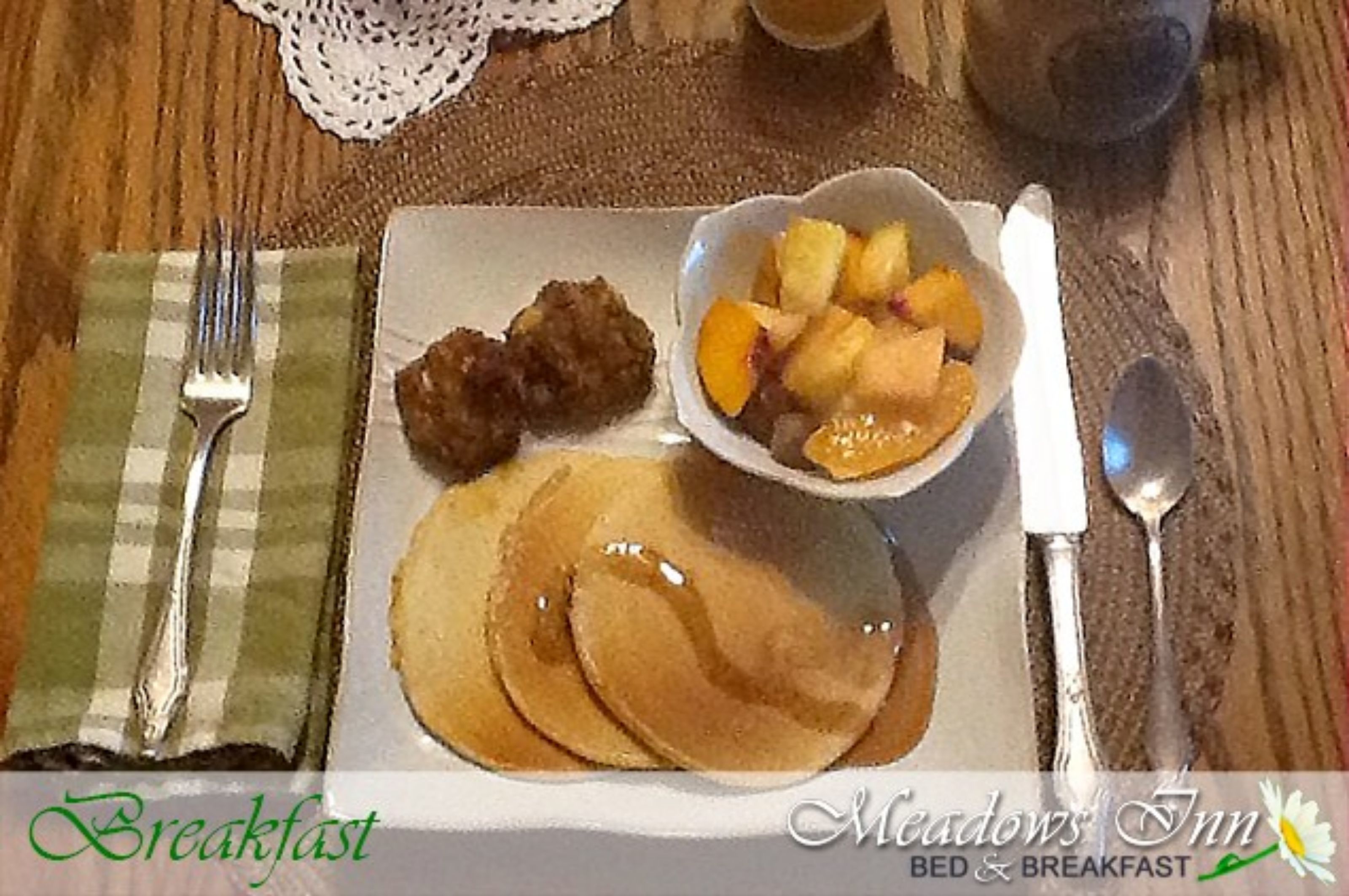 Prato de café da manhã com panquecas, uma tigela de frutas e uma porção pequena de carne.