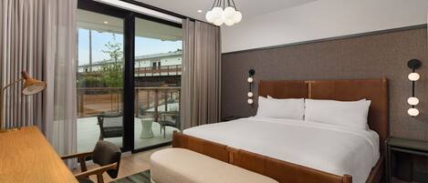 A modern hotel room with a large bed, a desk, a chair, and a view of the outdoors.