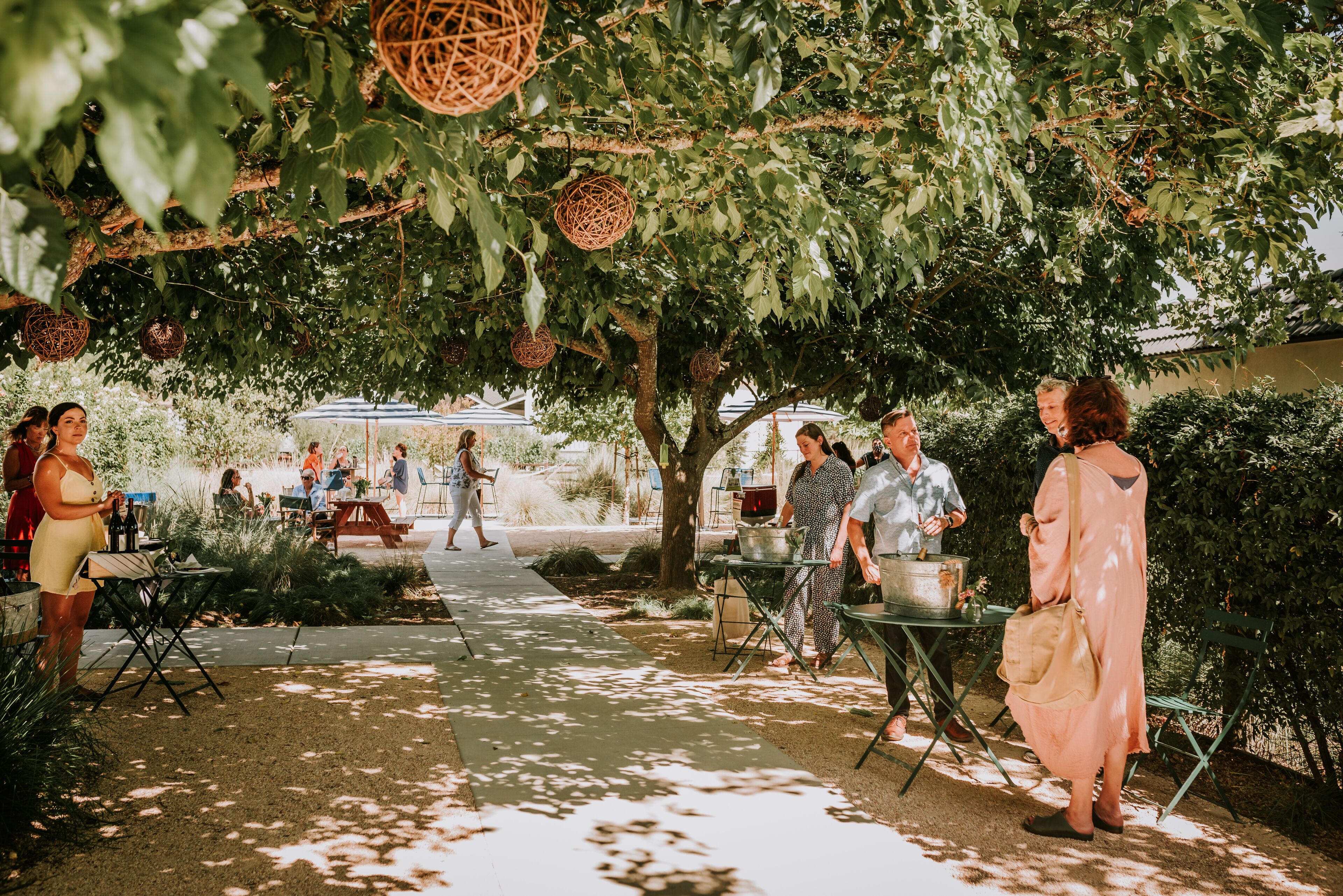 An outdoor patio area with tables and chairs, surrounded by greenery and hanging decorations.