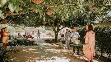 An outdoor patio area with tables and chairs, surrounded by greenery and hanging decorations.