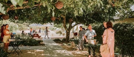 An outdoor patio area with tables and chairs, surrounded by greenery and hanging decorations.