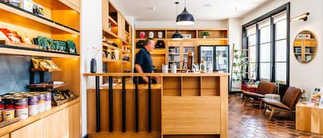 Un interior moderno con estantes de madera llenos de aperitivos y bebidas, una barra central y un suelo con baldosas hexagonales.
