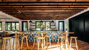 A bar area with wooden stools and a central bar counter, large windows, and a herringbone tile floor. - Calistoga Motor Lodge and Spa (Calistoga)