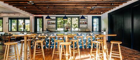A bar area with wooden stools and a central bar counter, large windows, and a herringbone tile floor.