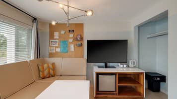 A modern living room with a sofa, a flat-screen TV, a coffee station, and a corkboard with notes.