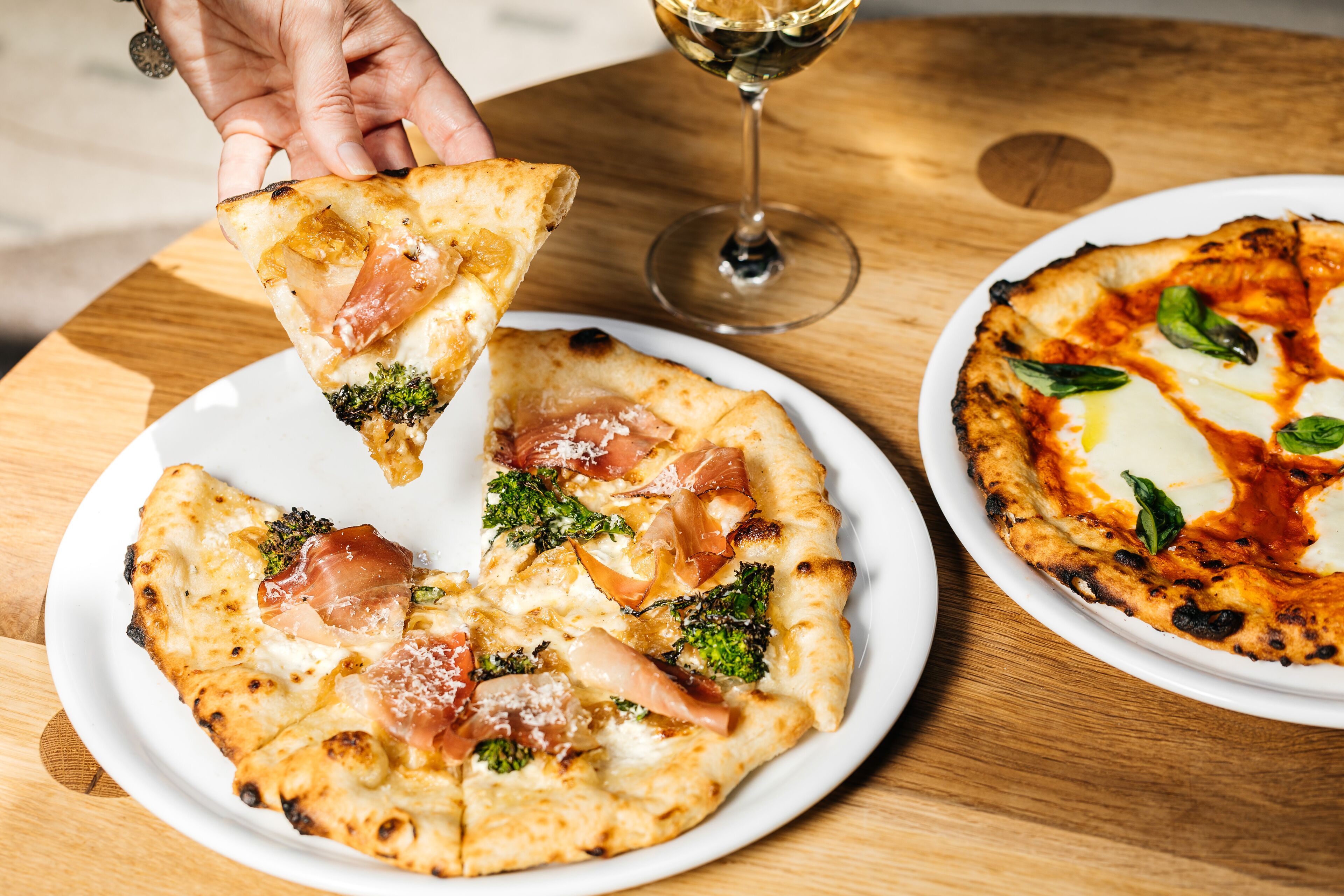A pizza with toppings and a glass of white wine on a wooden table.