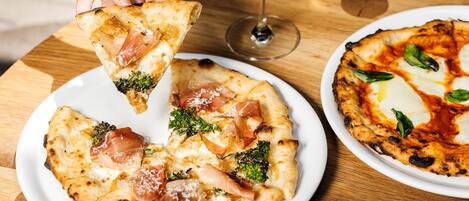 A pizza with toppings and a glass of white wine on a wooden table.
