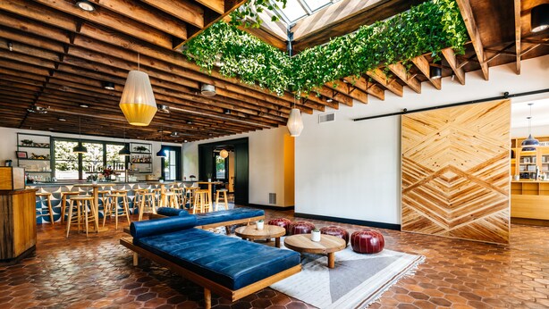 A modern interior with a wooden ceiling, a blue sofa, round tables, and a green wall with plants. - Calistoga Motor Lodge and Spa (Calistoga)