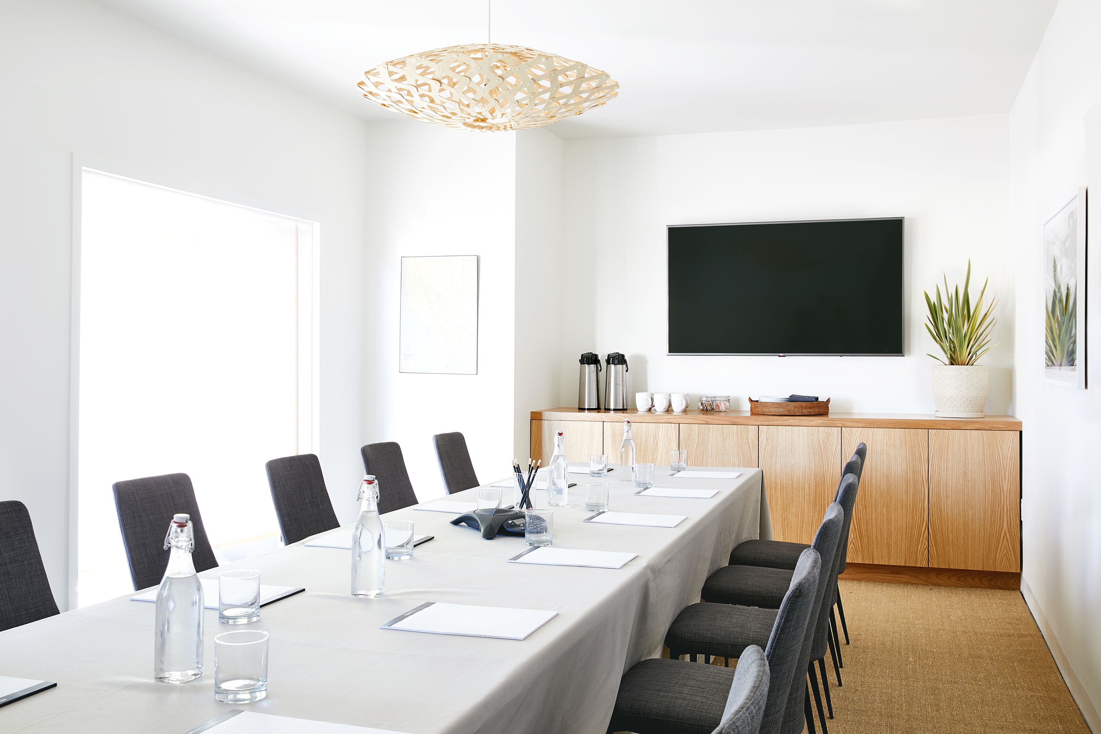 Un salón de conferencias con una larga mesa, sillas, un televisor y un armario con electrodomésticos de cocina.