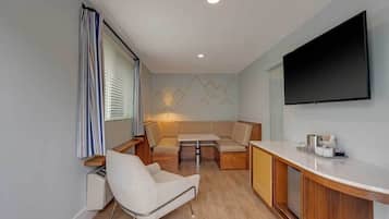 A compact living space with a sofa, a chair, a small table, and a flat-screen TV mounted on the wall.